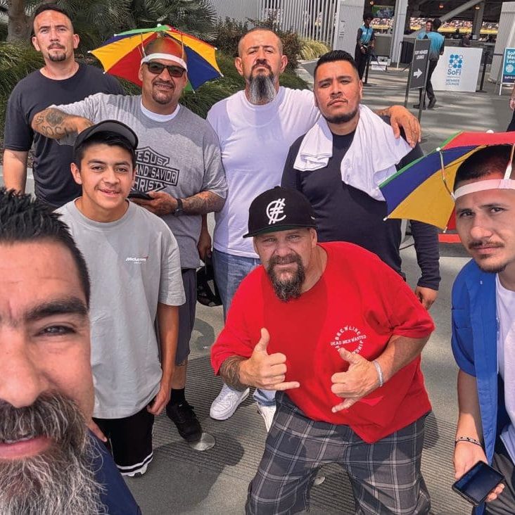 A group of men, some wearing rainbow umbrellas on their heads, pose together outdoors like a team of vibrant Rams with renewed hope.